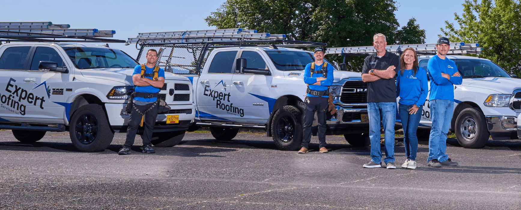 The Expert Roofing Services team stands in front of trucks.